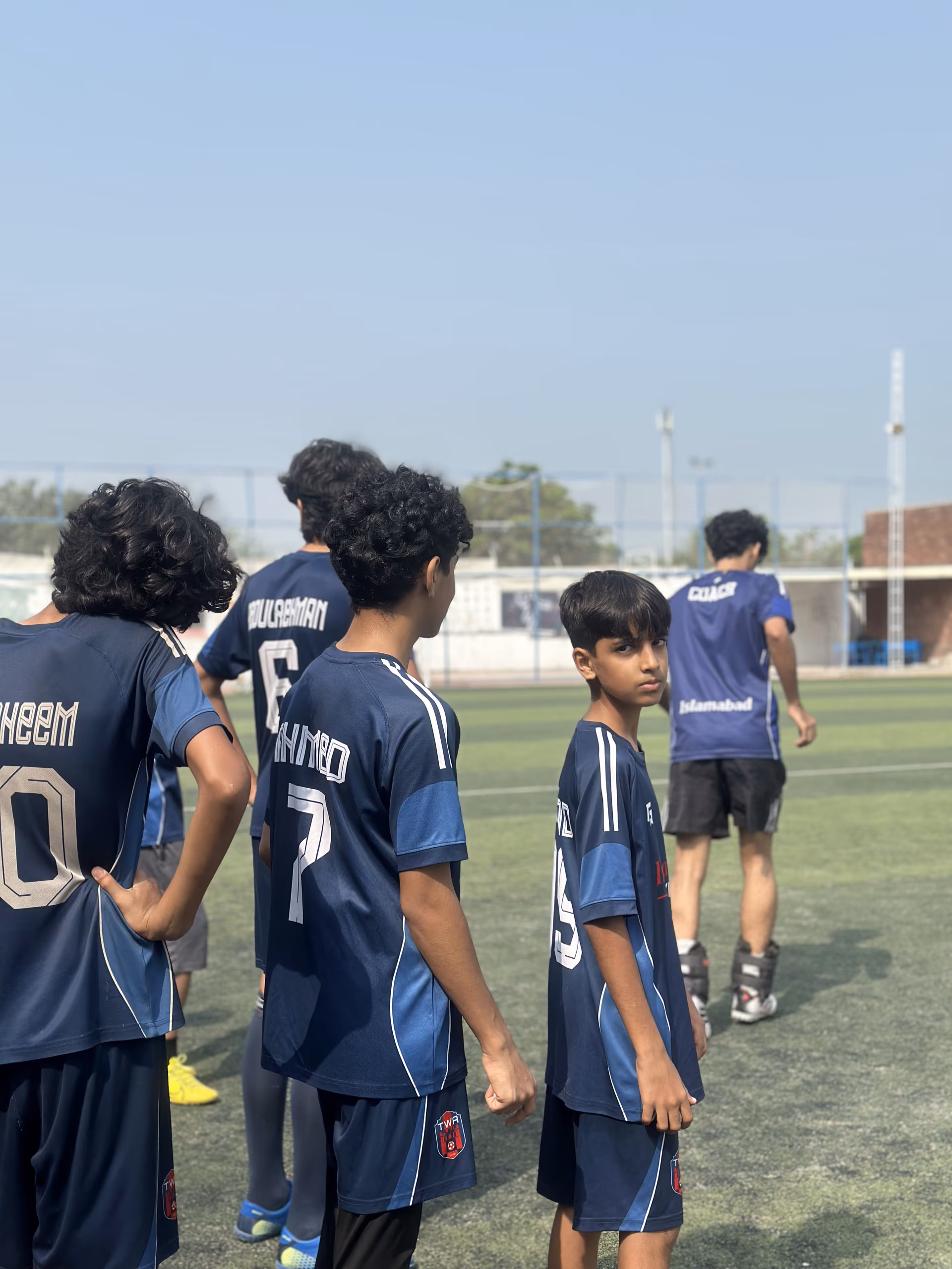 The squad in a huddle, backs to camera, numbers showing on the navy shirts